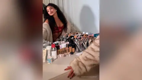 Woman in a cozy beige cardigan sitting at a vanity filled with professional makeup brushes and skincare products.