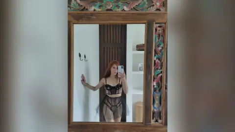 LaurentBelluci poses for a mirror selfie wearing a black lace bra and sheer black panties against a white wall.