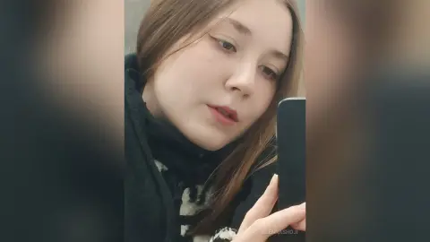 Young woman with long brown hair wearing a black hooded sweatshirt taking a moody selfie indoors.