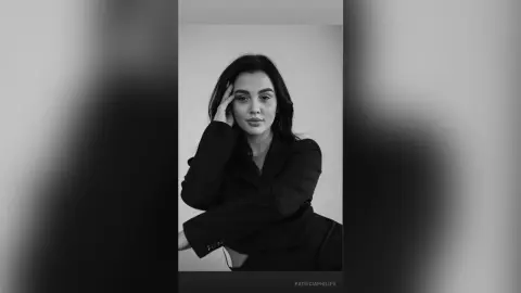 Moody black and white portrait of a woman in a stylish black blazer posing against a neutral background.