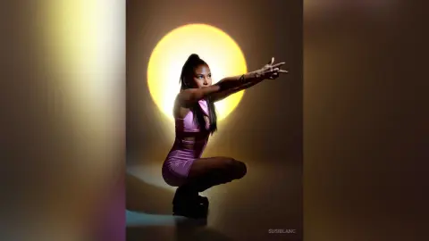 Fashionable woman in a pink outfit posing against a glowing yellow moon backdrop in a moody studio setting.