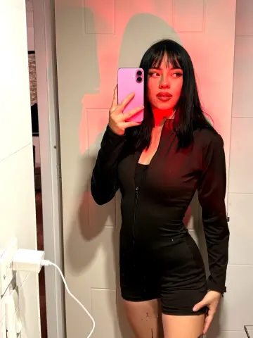 Young woman in a black long-sleeve bodysuit taking a moody selfie in red lighting.