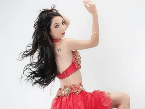 Beautiful belly dancer in a red sequined costume performing a graceful dance against a white background.