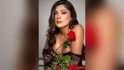 Glamorous woman in a black lace outfit holding a red rose against a neutral studio background.