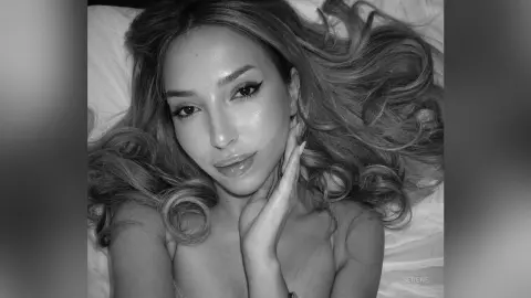 Beautiful woman with long wavy hair relaxing on a white bed in a serene black and white portrait.