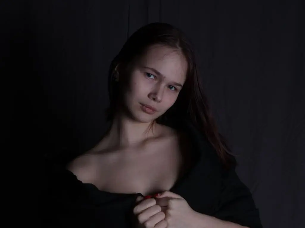 Young woman in a black off-the-shoulder top posing with a moody, cinematic expression against a dark background.