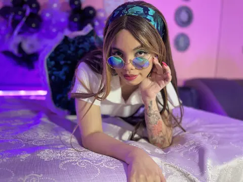 maaeve_elf — Young woman in white shirt and blue headband wearing sunglasses while lying on a bed in purple mood lighting.