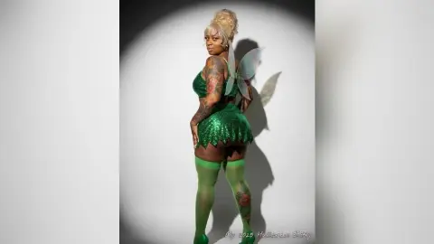 Curvy woman in a sparkling green fairy costume and tights posing against a white studio background.