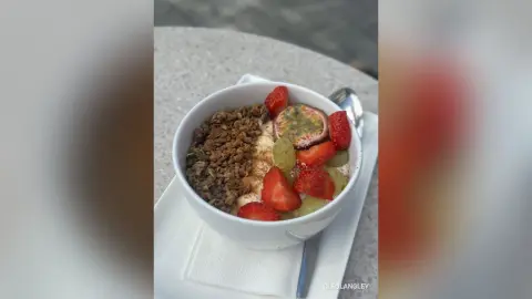 Healthy breakfast granola bowl topped with fresh strawberries and passion fruit on a white napkin.