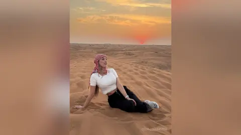Stylish woman in white top and red headscarf relaxing in the desert dunes during a golden sunset.