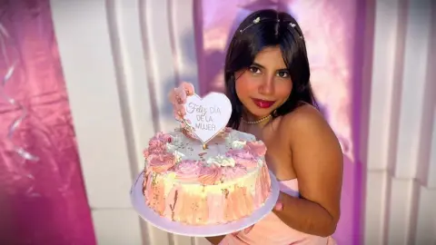 Smiling woman in a pink dress holding a celebratory International Women's Day cake in a festive setting.