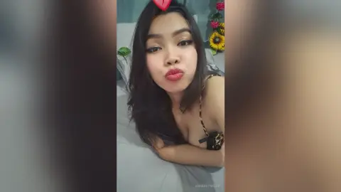 Young woman in a leopard print bikini top blowing a kiss while relaxing on a bed in a cozy bedroom setting.