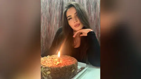 Young woman in a black top celebrating a birthday with a lit chocolate cake in a cozy indoor setting.