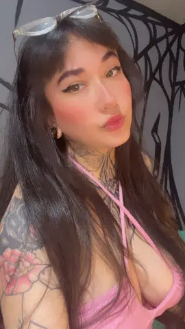 SallyLynn18 is a long-haired brunette with tattoos wearing a pink top and glasses on her head.