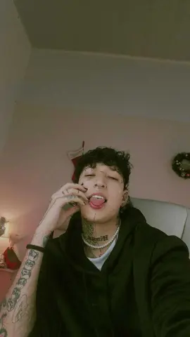 lucirosee sticks out his tongue while wearing a black hoodie and a pearl necklace, showing off his facial tattoos and arm tattoos.