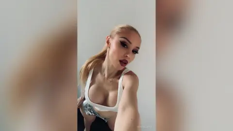 KendallMinx poses in a white tank top and sparkly bottoms, showing off her cleavage and blonde hair.