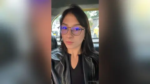 Young woman with glasses and nose ring wearing a black leather jacket sitting in a car with a moody vibe.