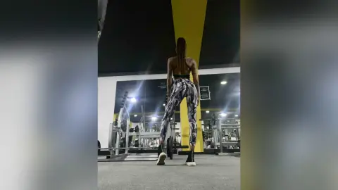Athletic woman in patterned leggings and sports bra stretching in a modern gym setting.