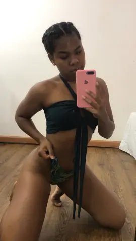 Young woman in dark green bikini posing for a mirror selfie in a cozy indoor setting.