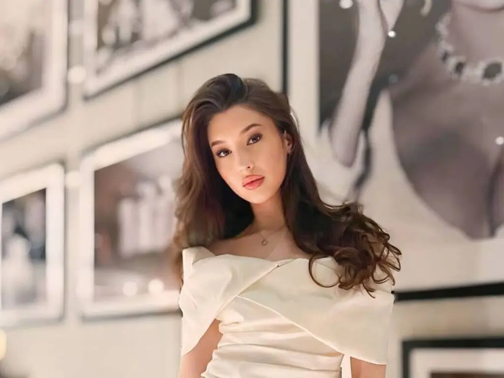 Elegant woman in a white satin off-the-shoulder dress posing in a modern art gallery setting.