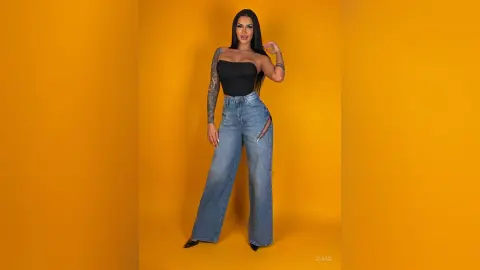 Smiling woman in a black tube top and high-waisted blue jeans posing against a vibrant yellow background.