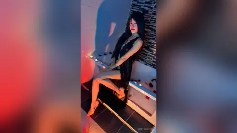 Elegant woman in a black lace dress sitting in a moody, dimly lit modern bathroom with red ambient lighting.