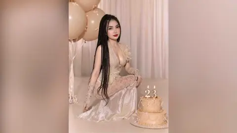 Young woman with long braids in a white lace gown celebrating her 23rd birthday with a cake and balloons.