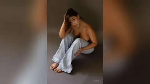 Young woman in light blue denim jeans sitting on a studio floor with a relaxed, moody aesthetic.