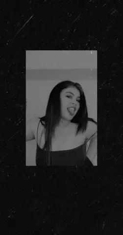 Moody black and white portrait of a young woman in a dark camisole sticking her tongue out playfully.