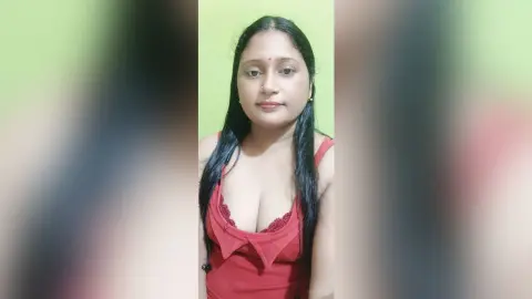 QueenPori wears a low-cut red top while looking directly at the camera against a plain green wall.