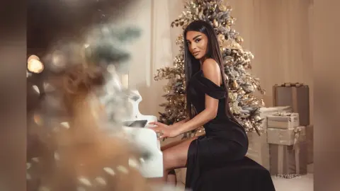 Elegant woman in a black evening dress playing a white piano near a glowing Christmas tree in a festive mood.