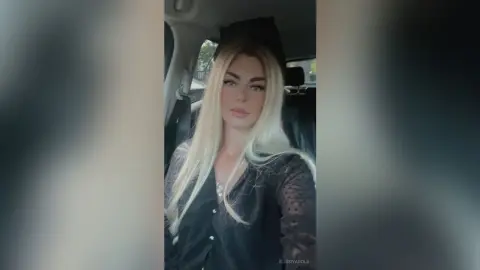 Blonde woman in a black lace blouse sitting in a car with a soft, glamorous mood.