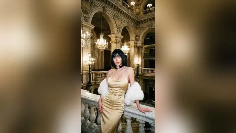 Elegant woman in a gold satin gown and white fur stole posing in a luxurious classical ballroom.