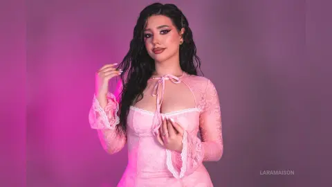 Young woman with long dark hair wearing a pink lace dress against a soft purple studio background.