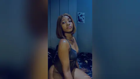 JoanJon poses in a dark room wearing a grey lace bra and black panties while looking at the camera.