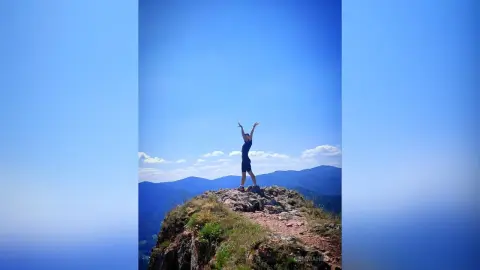 Joyful traveler with arms raised on a rocky mountain peak under a clear blue sky.