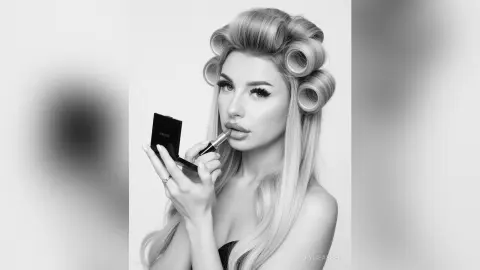 Glamorous blonde woman applying dark lipstick in a black and white beauty portrait.