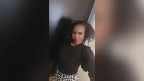 Smiling woman in a black long-sleeve top and patterned skirt posing in a modern indoor setting.
