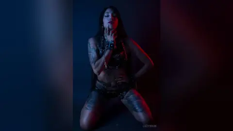 Moody portrait of a tattooed woman in edgy black streetwear posing under dramatic blue and red lighting.
