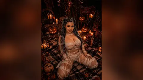 Woman in a mummy costume sitting amidst glowing jack-o'-lanterns for a spooky Halloween night mood.