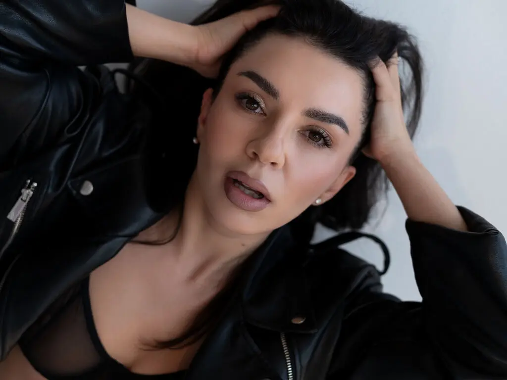 Moody portrait of a woman in a black leather jacket with dark hair against a white background.
