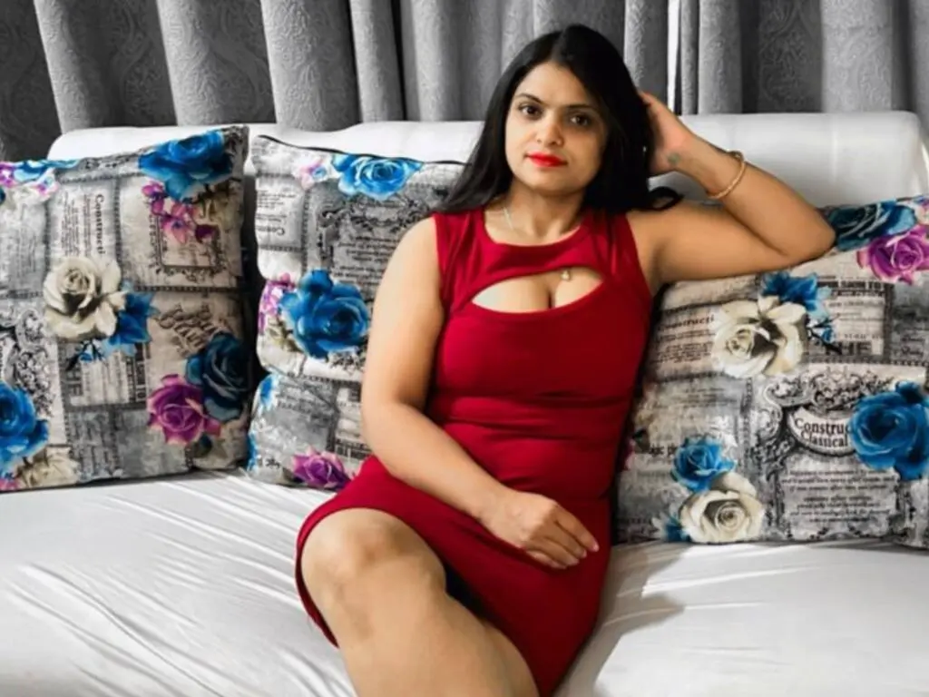 Woman in a red sleeveless dress sitting on a floral patterned sofa in a bright room.