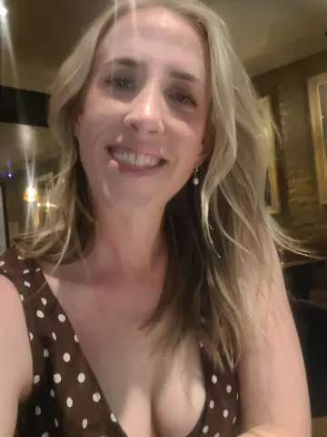 Smiling blonde woman in a brown polka dot dress enjoying a night out at a dimly lit restaurant.