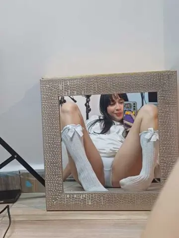 Young woman in white loungewear and high socks taking a selfie in a gold framed mirror.