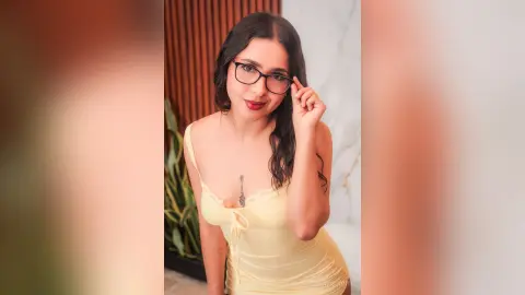 Smiling woman in a yellow camisole tank top wearing black glasses in a bright modern indoor setting.