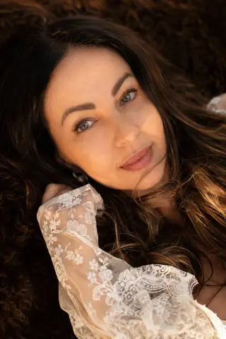 Beautiful woman in a white lace outfit lying in soft golden sunlight for a romantic, dreamy portrait.
