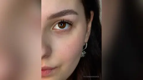 Close-up portrait of a young woman with brown eyes and natural makeup looking thoughtfully into the camera.