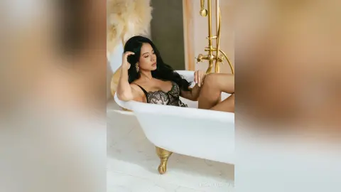 Elegant woman in black lace lingerie relaxing in a luxury white bathtub in a bright, modern bathroom.