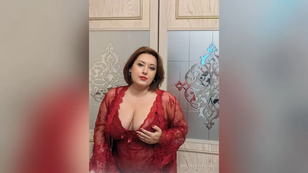 Woman with brown hair and red lipstick wearing a red lace outfit in a cozy indoor setting.