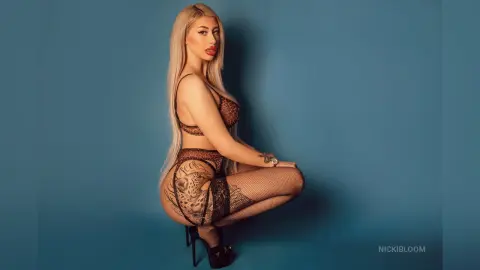 ViviAnne — NickiBloom poses in black lace lingerie and fishnet stockings against a blue background.